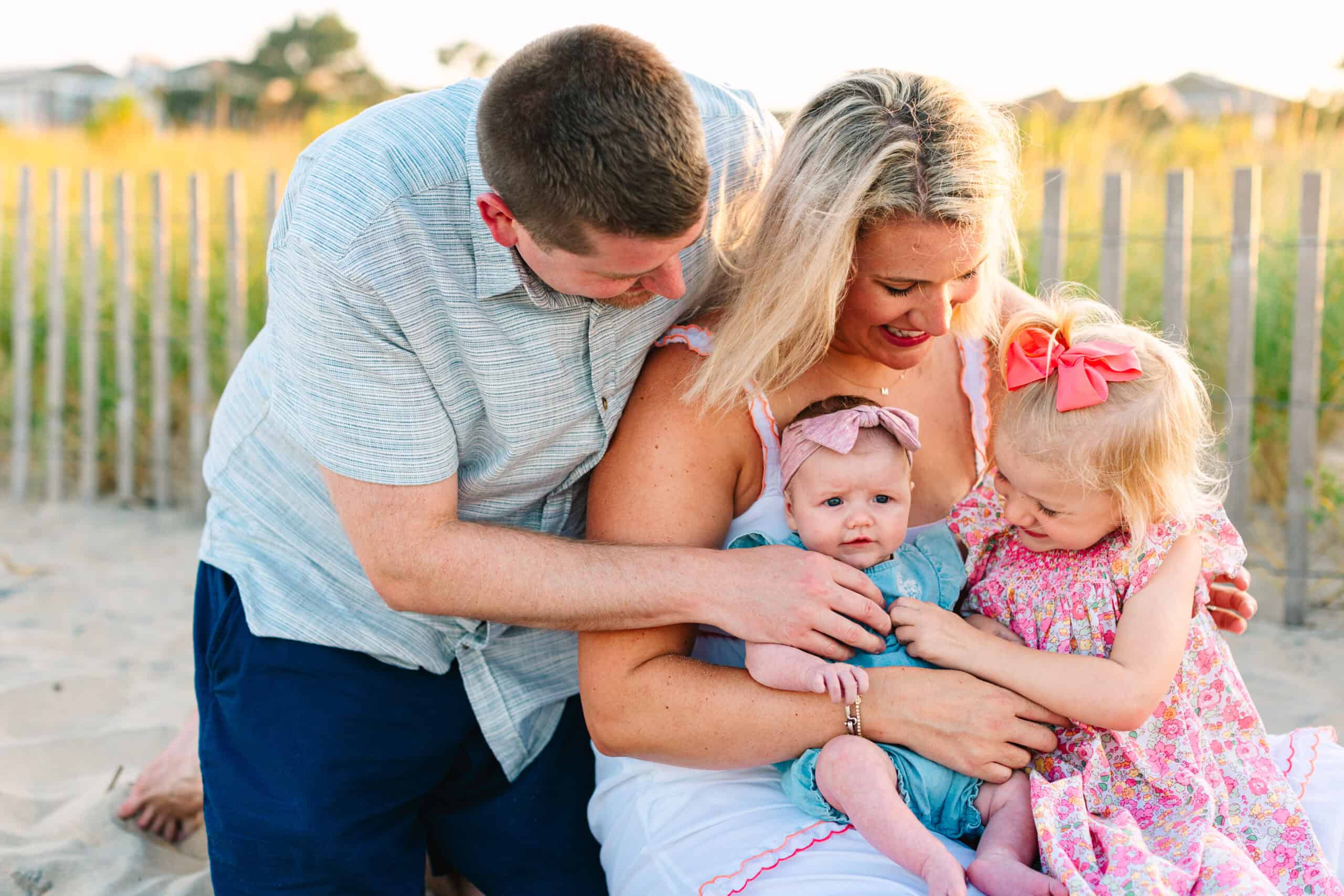 Family enjoying tender moment at the beach, vibrant sunset lighting in the background.